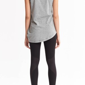 May include: A woman is wearing a gray sleeveless shirt and black leggings with mesh panels. The leggings have a high waist and a fitted silhouette.