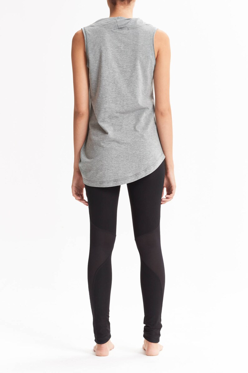 May include: A woman is wearing a gray sleeveless shirt and black leggings with mesh panels. The leggings have a high waist and a fitted silhouette.