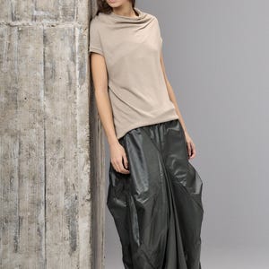 May include: A woman's outfit featuring a brown felt bucket hat, a beige short-sleeved top, and a dark green, voluminous skirt. The outfit has a minimalist, modern aesthetic, with a focus on texture and shape.