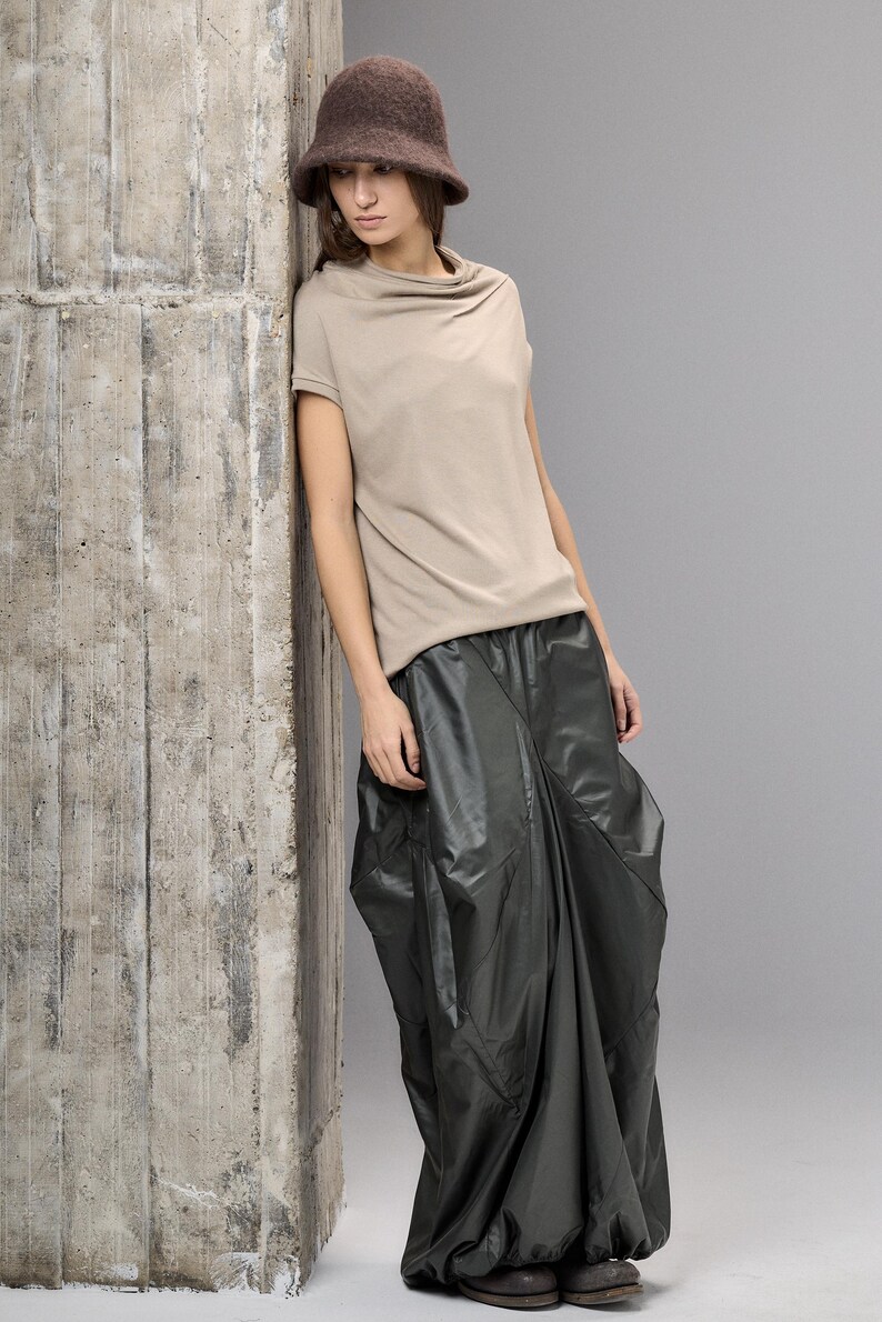 May include: A woman's outfit featuring a brown felt bucket hat, a beige short-sleeved top, and a dark green, voluminous skirt. The outfit has a minimalist, modern aesthetic, with a focus on texture and shape.