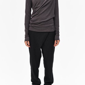 Puede incluir: Una camisa gris de cuello alto de manga larga con un dise&ntilde;o drapeado y pantalones negros. La persona lleva botas negras de tobillo.