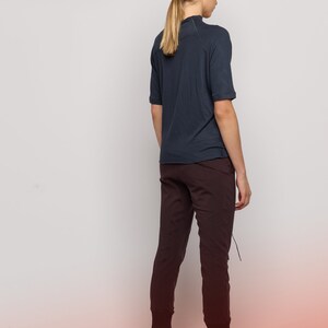 May include: A woman wearing a dark blue short-sleeved shirt and dark brown pants. She is standing with her back to the camera and her hair is pulled back in a ponytail.