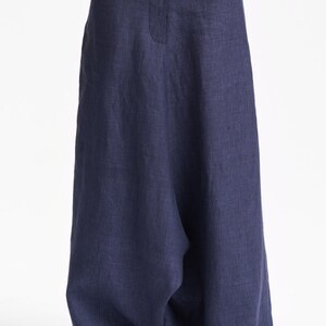 May include: Wide-leg trousers in a deep navy blue color featuring a high-waisted design with a central vertical seam detail. The garment is crafted from a textured fabric and falls in a loose, relaxed silhouette that extends down to the ankles.