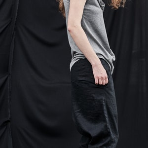 May include: A woman wearing a gray sleeveless top and black pants. The top has a cowl neck and the pants are loose fitting.