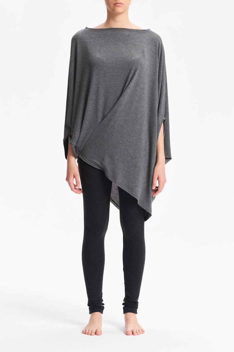 K&ouml;nnte beinhalten: Eine Frau tr&auml;gt ein graues, asymmetrisches, lang&auml;rmeliges Oberteil mit schwarzen Leggings.
