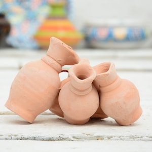 Può includere: Quattro piccoli vasi in terracotta, impilati e disposti in un gruppo. I vasi sono di colore marrone chiaro e hanno un aspetto rustico e fatto a mano.