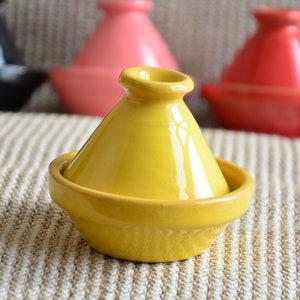 May include: A yellow ceramic tagine with a lid. The tagine is a traditional Moroccan cooking pot.