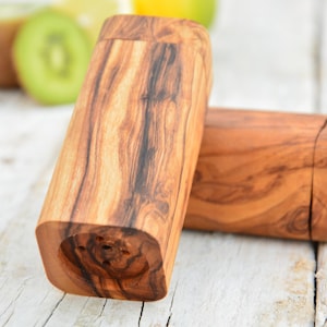 Könnte beinhalten: Zwei Salz- und Pfefferstreuer aus Olivenholz. Die Streuer sind rechteckig und haben eine natürliche Holzoptik. Die Streuer stehen auf einer weißen Holzoberfläche.