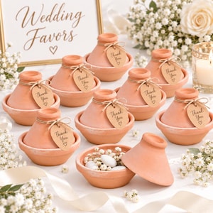 Puede incluir: Una colección de pequeños recipientes de arcilla color terracota con forma de tajine. Cada pieza cuenta con una tapa cónica y una base redonda, atadas con un cordel marrón y una etiqueta de papel en forma de lágrima con el texto Thank You y un corazón.