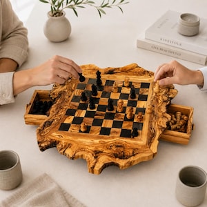 Könnte beinhalten: Ein Schachspiel mit einem Brett aus einer natürlichen Olivenholzplatte mit Baumkante und einem Muster aus dunklen und hellen Feldern. Das Brett enthält zwei integrierte Schubladen an gegenüberliegenden Seiten zur Aufbewahrung der Figuren.
