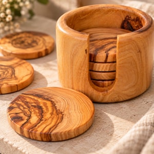 Op de afbeelding: Een set ronde houten onderzetters met een duidelijk natuurlijk nerfpatroon, inclusief een bijpassende cilindrische houder met een verticale uitsparing. De onderzetters zijn gemaakt van lichtbruin hout met donkerbruine, wervelende nerfdetails.