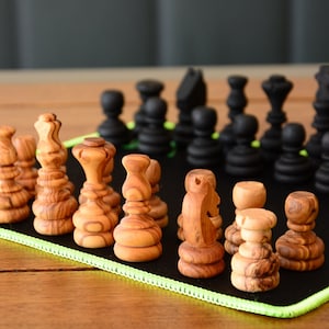 Peut inclure: Un jeu d'échecs en bois sur un plateau en feutre vert et noir. Les pièces sont en bois brun clair avec un motif de grain naturel. Les pièces sont disposées en formation de jeu, les pièces blanches à gauche et les pièces noires à droite.
