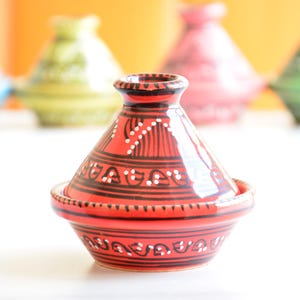 Könnte beinhalten: Eine rote und schwarze Keramik-Tagine mit weißen geometrischen Mustern. Die Tagine ist ein traditioneller marokkanischer Kochtopf mit einem konischen Deckel.