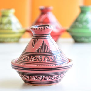 Può includere: Un set di cinque tagine in ceramica colorate con intricati disegni in bianco e nero. Le tagine sono disposte in fila su una superficie bianca.