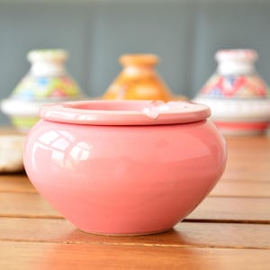 Könnte beinhalten: Ein runder Aschenbecher aus rosa Keramik mit leicht erhöhtem Rand. Der Aschenbecher steht auf einer Holzoberfläche.
