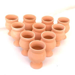 Könnte beinhalten: Eine Ansammlung von elf kleinen, unglasierten Terrakotta-Töpfen, die in einer dreieckigen Form angeordnet sind. Jeder Topf hat einen abgerundeten Körper, einen ausgestellten Rand und einen Sockel. Die Töpfe haben einen warmen, erdigen Farbton.