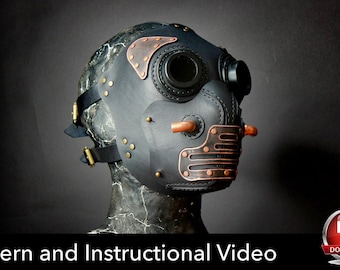 May include: A black mask featuring copper-colored metal accents, including circular eye lenses, side pipes, and a slotted mouth guard. The mask is secured with black straps and brass-toned buckles, displayed on a dark, textured mannequin head.