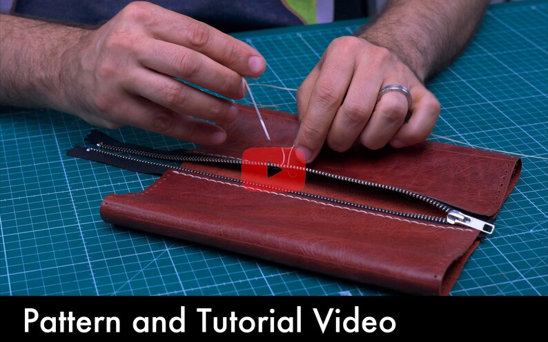 Może przedstawiać: Osoba przyszywa zamek błyskawiczny do brązowego sk&oacute;rzanego portfela. Portfel leży na zielonej macie do cięcia. Tekst "Pattern and Tutorial Video" znajduje się na dole obrazu.