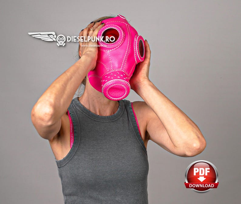 May include: A pink leather gas mask with white stitching and round eye holes. The mask is being worn by a person.