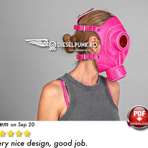 May include: A pink leather gas mask with a white strap and a large round eye hole. The mask has a white stitched design and a white logo on the side that says "DIESELPUNK.RO".