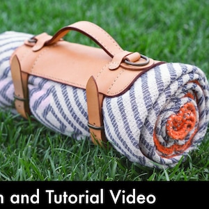 May include: A rolled woven blanket featuring a white and dark blue chevron pattern with an orange center, secured by a tan leather carrier strap with a handle and metal hardware. The image includes a red circular icon with the text PDF DOWNLOAD.