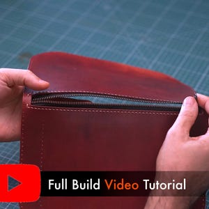 May include: A burgundy leather bag with a zipper closure is held open, revealing the interior. The bag is being held by two hands. The text "Full Build Video Tutorial" is displayed in white text on a black bar.
