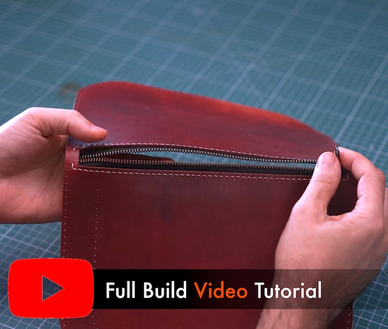 May include: A burgundy leather bag with a zipper closure is held open, revealing the interior. The bag is being held by two hands. The text "Full Build Video Tutorial" is displayed in white text on a black bar.