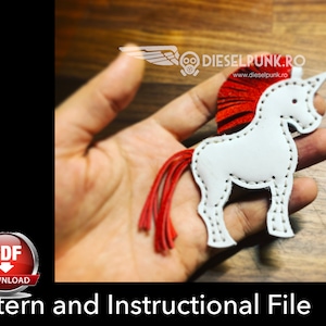 Puede incluir: Un unicornio de cuero blanco con una crin y cola rojas. El unicornio está cosido con hilo blanco. El unicornio está sostenido en una mano. La imagen incluye el texto "DIESELPUNK.RO" y "www.dieselpunk.ro".