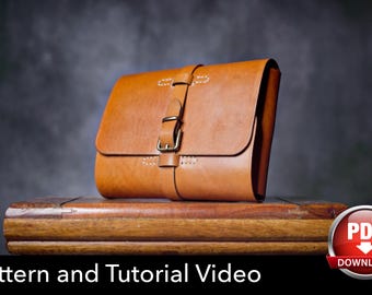 May include: A tan leather satchel with a front flap, a vertical strap, and a metal buckle closure. The bag features visible light-colored stitching along the flap and strap. The text "Pattern and Tutorial Video" and a PDF download icon are present.