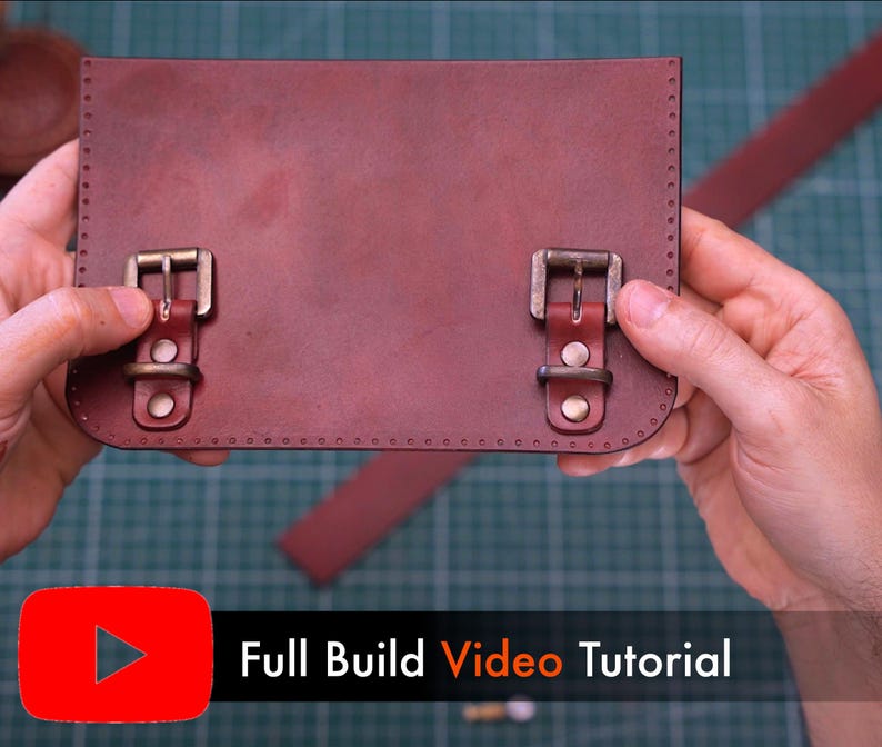 May include: A reddish-brown leather satchel with two brass buckles. The satchel is held by hands, with a strap visible in the background. The image includes a YouTube logo and the text "Full Build Video Tutorial".