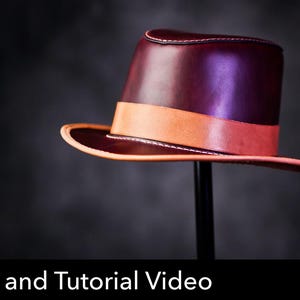 May include: A deep burgundy leather fedora hat featuring a smooth finish, a wide tan leather band around the crown, and a matching tan leather edge trim along the brim. The text Pattern and Tutorial Video is displayed at the bottom.