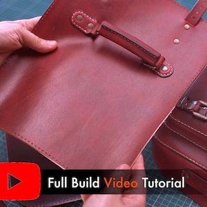 May include: A close-up of a burgundy leather satchel with a handle and strap attachments. The satchel is held open, revealing the interior. The text "Full Build Video Tutorial" is displayed in white on a black background.