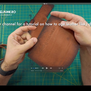 May include: A close-up of a brown leather pouch with a logo and the text "DIESELPUNK.RO". The text "check out my channel for a tutorial on how to age leather like I did" is also visible. The pouch is being held.