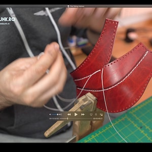 May include: A person is sewing two pieces of red leather together with white thread. The leather is clamped in a vise. The person is wearing a gray hoodie with the text "DIESELPUNK.RO" and the website address "www.dieselpunk.ro".