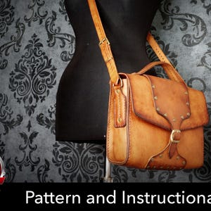 May include: A tan leather satchel with a top handle and an adjustable shoulder strap. The bag features a front flap secured by a metal buckle, decorative metal studs along the edges, and a structured rectangular body with visible stitching.