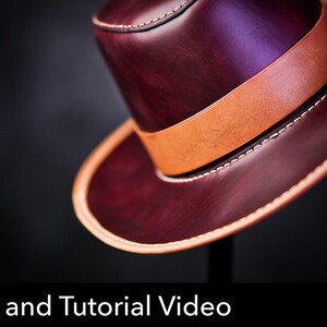 May include: A deep burgundy leather hat featuring a wide tan leather band around the crown and tan leather trim along the edge of the brim. The hat is accented with visible white stitching. Text at the bottom reads Pattern and Tutorial Video.