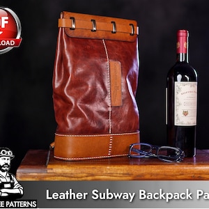 May include: A brown leather backpack with a structured base and a top flap secured by metal hardware. A vertical white stitch runs down the center. Beside it sits a bottle of red wine with a white label and a pair of blue-rimmed eyeglasses.