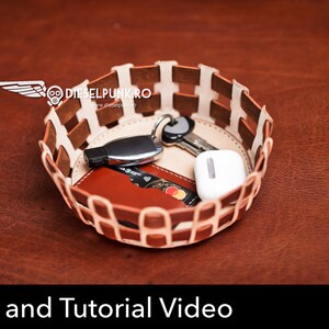 K&ouml;nnte beinhalten: Ein brauner Lederkorb mit einem wei&szlig;en geflochtenen Design. Der Korb ist mit verschiedenen Gegenst&auml;nden gef&uuml;llt, darunter Schl&uuml;ssel, ein USB-Stick, eine Kreditkarte und ein kleines wei&szlig;es Ger&auml;t. Der Korb steht auf einer braunen Oberfl&auml;che. Muster und Tutorial-Video.