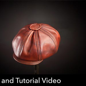 Può includere: Un berretto newsboy in pelle marrone con costruzione a otto pannelli, cuciture scure a vista e un bottone centrale. Il berretto presenta una visiera corta e curva. Sono visibili il testo "Pattern and Tutorial Video" e un'icona "PDF DOWNLOAD".