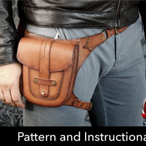 Può includere: Una borsa da gamba in pelle color cuoio con chiusura a patta, cinturino centrale, finiture in metallo color ottone e cuciture decorative lungo i bordi. La borsa è fissata con cinghie regolabili in vita e sulla coscia. Testo: PDF DOWNLOAD Pattern and Instructional Video.