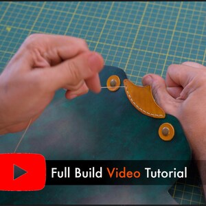 May include: Hands working on a leather project, stitching with thread. The leather is dark green with a tan accent piece. The image includes the text "Full Build Video Tutorial" with a YouTube logo.