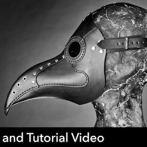May include: A black leather plague doctor mask with a long, curved beak, circular eye lenses, and silver-toned metal rivets along the seams. The mask features an adjustable leather strap with a metal buckle and is displayed on a textured head form.