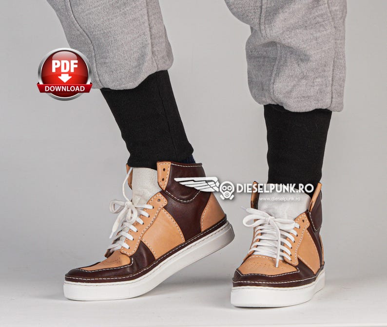 Puede incluir: Un par de zapatillas de ca&ntilde;a alta marrones y beige con cordones blancos. Las zapatillas tienen una suela blanca y una parte superior de cuero marr&oacute;n con un panel de cuero beige en el lateral. Las zapatillas las lleva puestas una persona que lleva pantalones de ch&aacute;ndal grises.