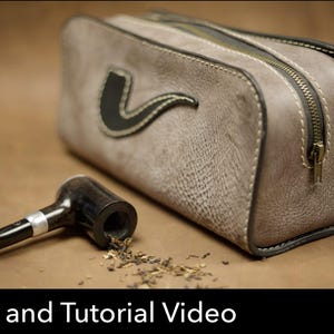 May include: A grey textured leather pouch with a zipper closure and a black pipe applique on the side, accompanied by a black smoking pipe with a silver band and loose tobacco. The image includes a red PDF download icon and the text Pattern and Tutorial Video.