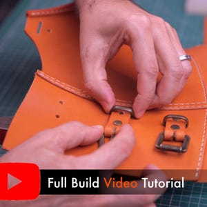 May include: An orange leather piece featuring white stitching, pre-punched holes, and attached bronze-colored metal buckles. A black banner at the bottom displays a red YouTube play icon and the white text Full Build Video Tutorial.