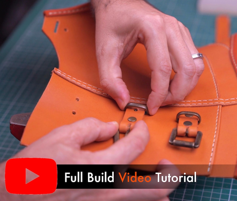 May include: An orange leather piece featuring white stitching, pre-punched holes, and attached bronze-colored metal buckles. A black banner at the bottom displays a red YouTube play icon and the white text Full Build Video Tutorial.