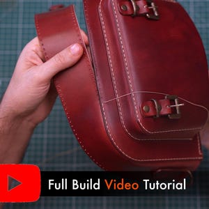 May include: A handcrafted, burgundy leather satchel with white stitching and brass buckles. The bag features a flap closure and a shoulder strap. The text "Full Build Video Tutorial" is displayed on the bottom of the image.