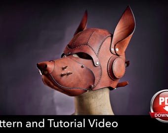 May include: A brown leather dog mask featuring pointed ears, metallic studs on the snout, and visible stitching along the panels. The mask is displayed on a mannequin head. Text at the bottom reads: Pattern and Tutorial Video with a PDF icon.