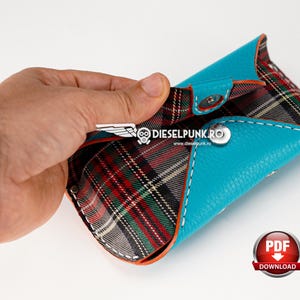 May include: A turquoise leather wallet with a red, black, and white plaid lining. The wallet is open and the lining is visible. The wallet has a snap closure and a small metal logo on the front.