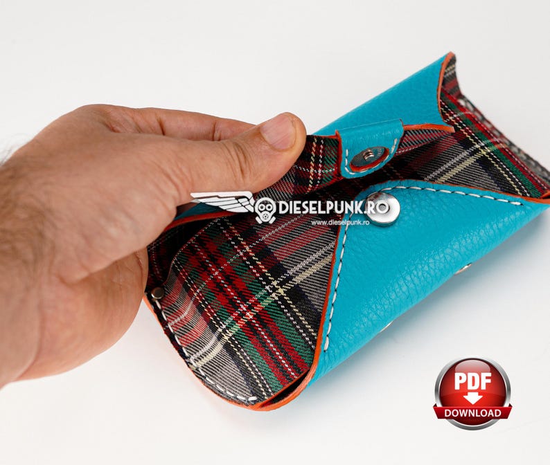 May include: A turquoise leather wallet with a red, black, and white plaid lining. The wallet is open and the lining is visible. The wallet has a snap closure and a small metal logo on the front.